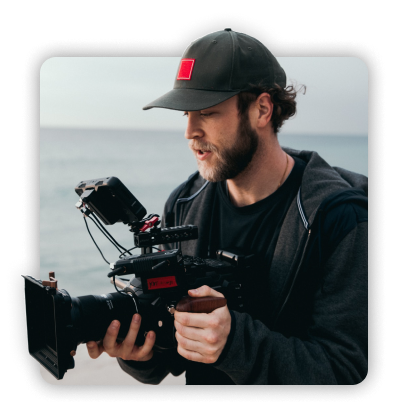 Man standing on the beach while operating a video camera.